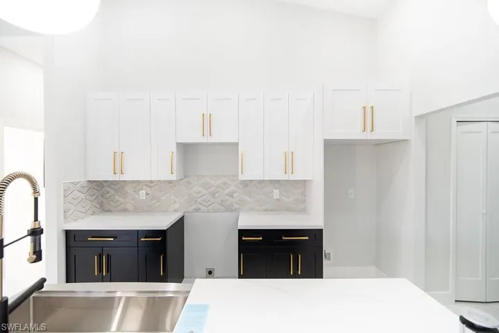Dual tone kitchen featuring a high ceiling, two tone color scheme, light stone countertops, and backsplash