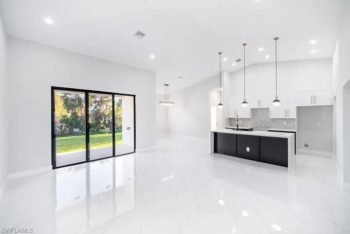 Dual tone kitchen featuring pendant lighting, a kitchen island with sink, decorative backsplash, open floor plan, and lofted ceiling