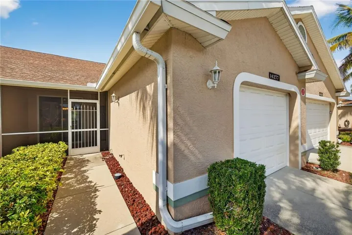 View of exterior entry with stucco siding, a garage, a sunroom, and concrete driveway