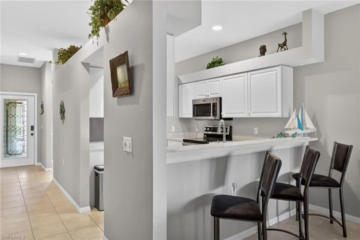 Kitchen with white cabinetry, light tile patterned floors, light countertops, appliances with stainless steel finishes, and a kitchen bar