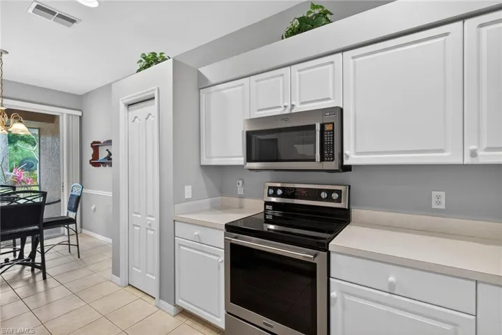 Kitchen with stainless steel appliances, white cabinets, light countertops, a chandelier, and light tile patterned floors