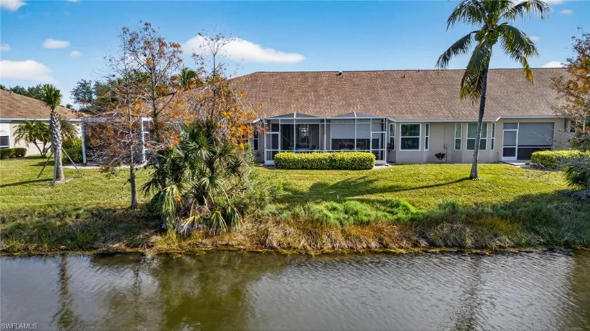 Rear view of property featuring a water view, a sunroom, a lawn, and a lanai