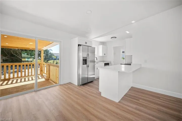 Kitchen featuring stainless steel fridge, white cabinets, a peninsula, light wood-style floors, and recessed lighting