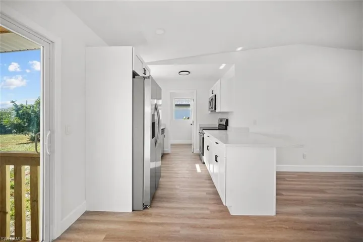Kitchen featuring a barn door, white cabinets, appliances with stainless steel finishes, light wood finished floors, and a peninsula