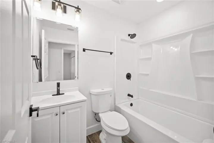 Full bathroom with shower / bath combination, vanity, and dark wood-style floors