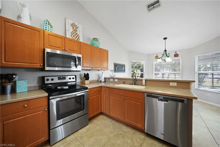 Kitchen with sink, stainless steel appliances, a notable chandelier, pendant lighting, and lofted ceiling