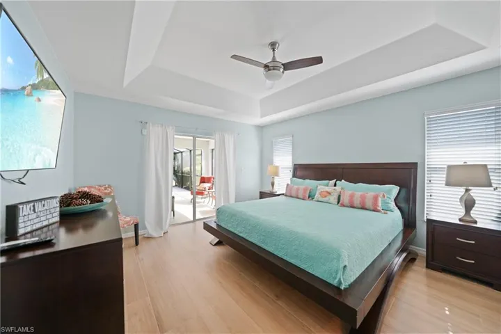 Bedroom featuring access to outside, light wood-type flooring, a tray ceiling, and ceiling fan