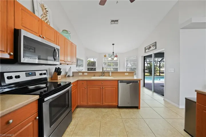 Kitchen with hanging light fixtures, sink, appliances with stainless steel finishes, and vaulted ceiling