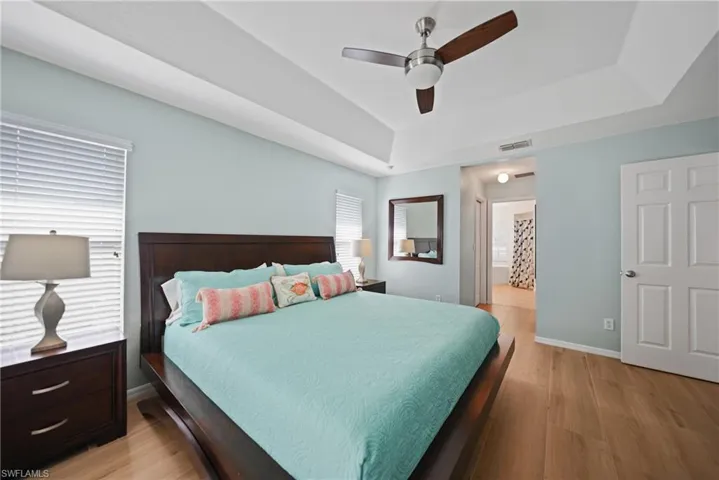 Bedroom with light hardwood / wood-style flooring, a raised ceiling, and ceiling fan