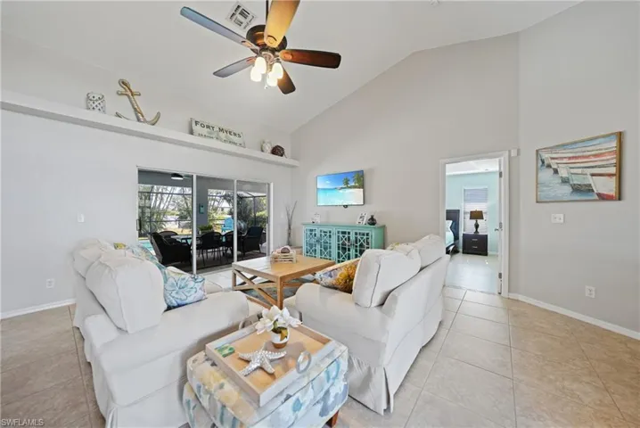 Living room with high vaulted ceiling, ceiling fan, and light tile patterned flooring