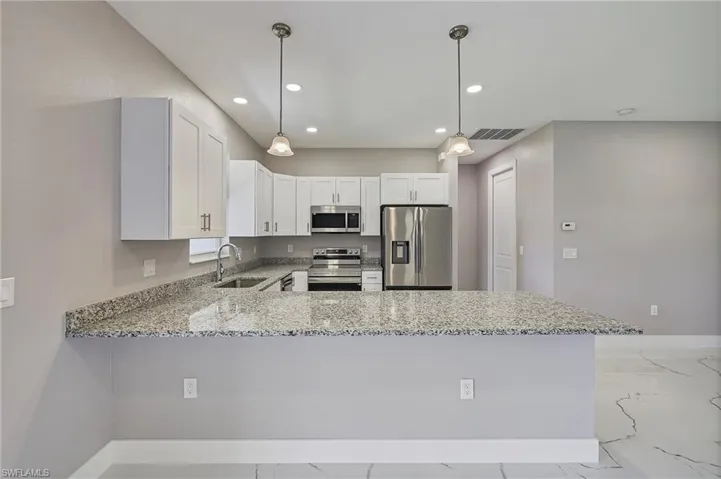 Kitchen with light stone countertops, a sink, white cabinets, stainless steel appliances, and recessed lighting