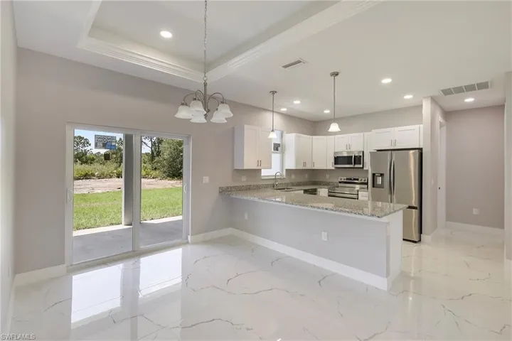 Kitchen featuring visible vents, a peninsula, light stone countertops, a sink, and stainless steel appliances