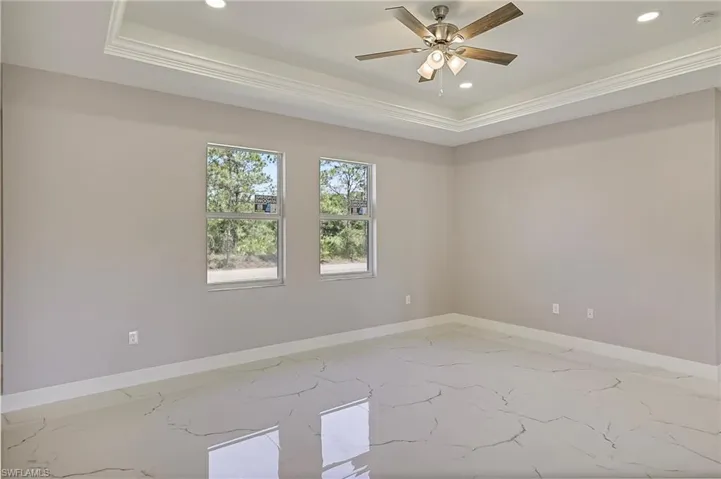 Unfurnished living room with ceiling fan, visible vents, crown molding, baseboards, and a tray ceiling