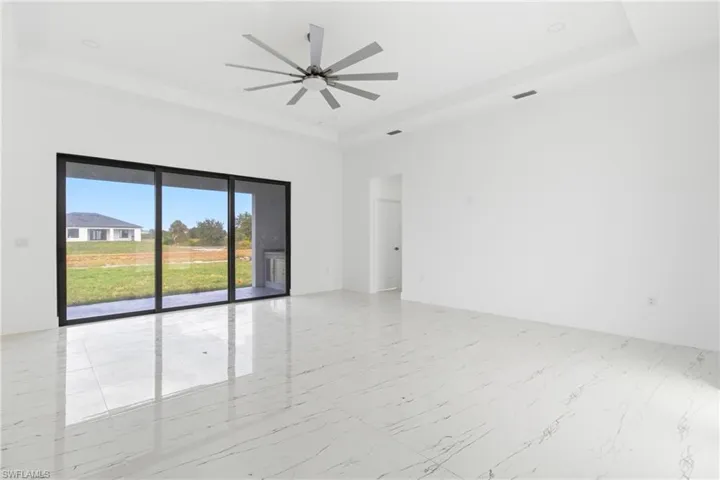 Spare room with a raised ceiling, a ceiling fan, and light marble finish flooring