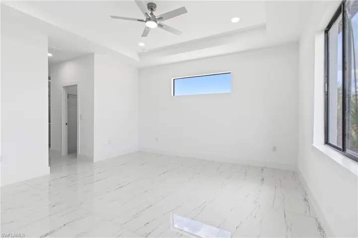 Spare room featuring light marble finish flooring, recessed lighting, a ceiling fan, and a raised ceiling