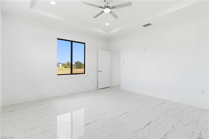 Unfurnished room featuring a tray ceiling, light marble finish floors, recessed lighting, and a ceiling fan