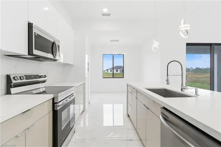 Kitchen featuring stainless steel appliances, modern cabinets, light marble finish flooring, and hanging light fixtures