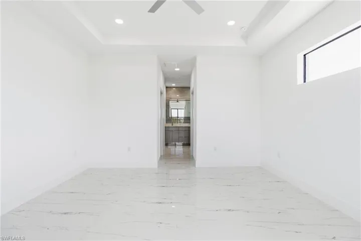 Empty room featuring recessed lighting, light marble finish flooring, a tray ceiling, and a ceiling fan