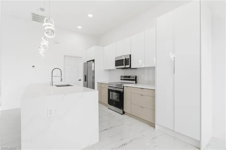 Kitchen with stainless steel appliances, hanging light fixtures, light stone countertops, light marble finish floors, and modern cabinets