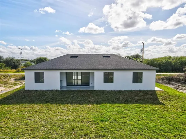 Rear view of property featuring stucco siding, a yard, a shingled roof, and a patio