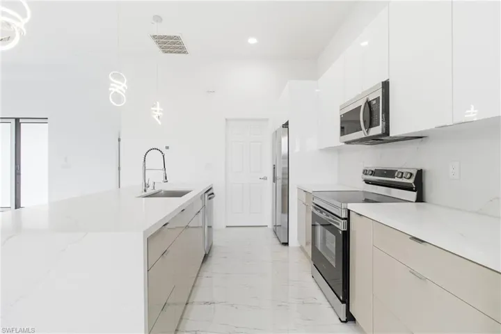 Kitchen featuring stainless steel appliances, pendant lighting, light stone countertops, and modern cabinets