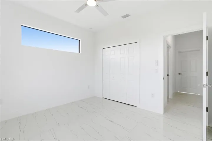 Unfurnished bedroom with light marble finish floors, ceiling fan, and a closet