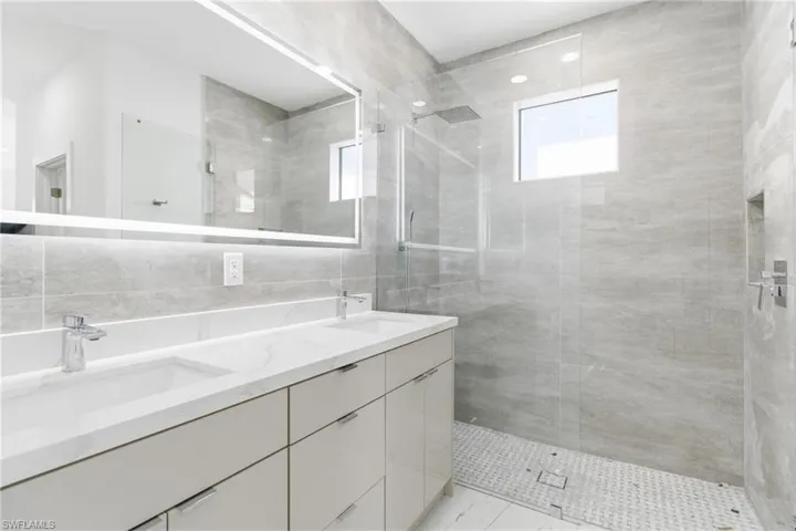 Full bath with double vanity, a walk in shower, and tile walls