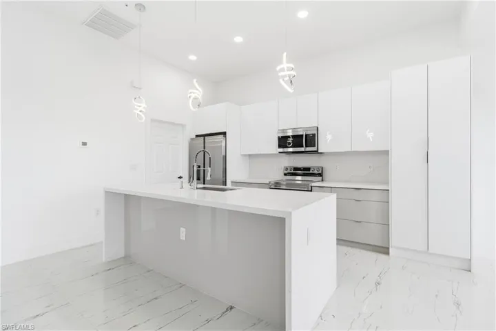 Kitchen with light marble finish floors, stainless steel appliances, pendant lighting, white cabinets, and light stone counters