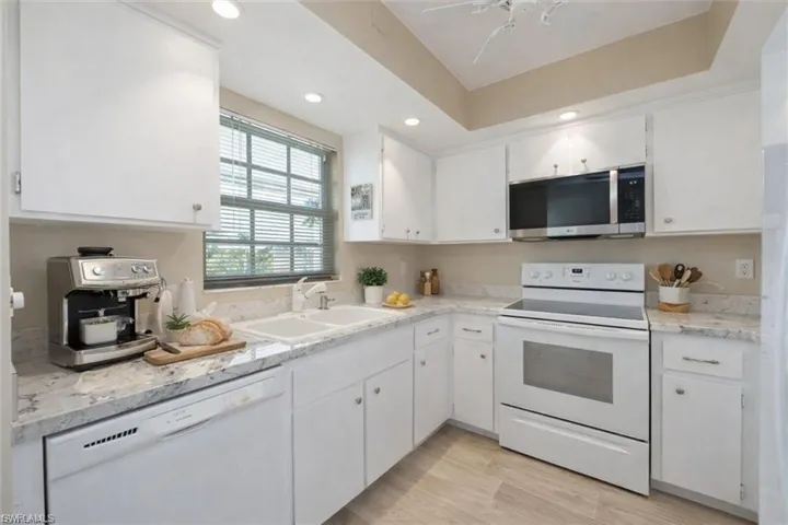 Virtually Staged Kitchen with white appliances, white cabinetry, recessed lighting, light stone counters, and a tray ceiling