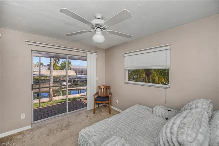 Carpeted bedroom with access to exterior, ceiling fan, and a water view