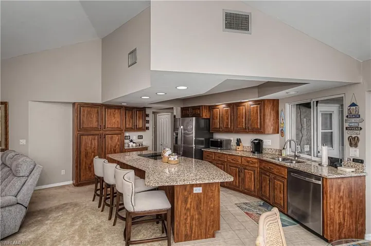 Kitchen featuring a kitchen island, light stone counters, stainless steel appliances, a kitchen breakfast bar, and vaulted ceiling
