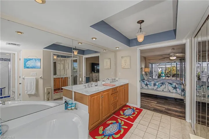 Bathroom featuring ensuite bath, double vanity, a tray ceiling, a garden tub, and a ceiling fan