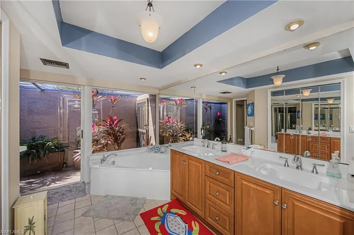 Bathroom with a tray ceiling, double vanity, light tile patterned floors, and a garden tub