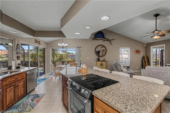 Kitchen with stainless steel appliances, light stone counters, a center island, suspended lighting, and vaulted ceiling
