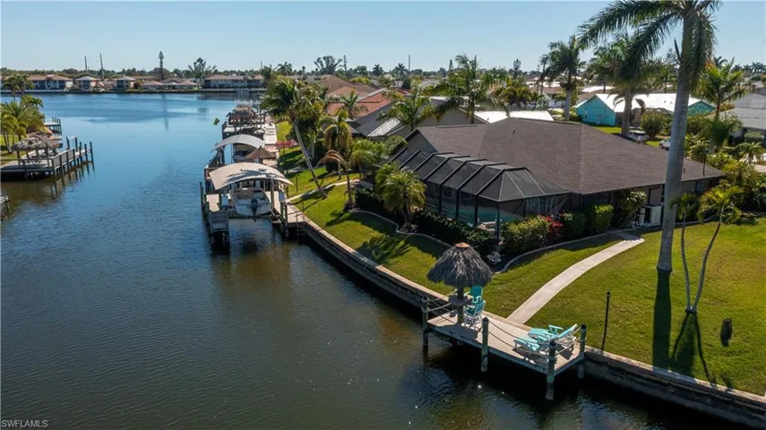 Dock area featuring boat lift, glass enclosure, a water view, and a lawn
