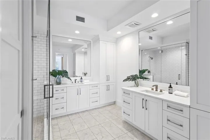 Bathroom featuring two vanities, a stall shower, light marble finish flooring, and recessed lighting