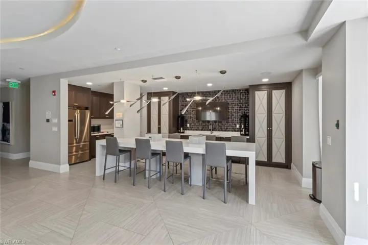 Clubroom Kitchen with dark brown cabinets, a spacious island, a kitchen breakfast bar, pendant lighting, and appliances with stainless steel finishes