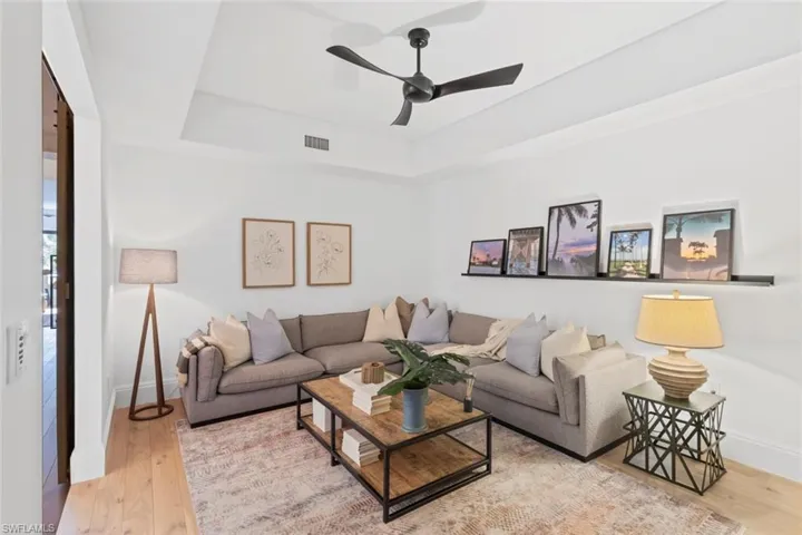 Living room featuring a raised ceiling, light wood-style flooring, and ceiling fan
