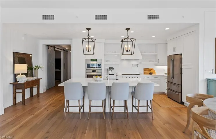 Kitchen featuring decorative light fixtures, a breakfast bar area, a barn door, white cabinets, and recessed lighting