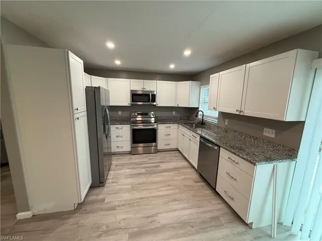 Kitchen with dark stone counters, stainless steel appliances, white cabinetry, light wood-type flooring, and recessed lighting
