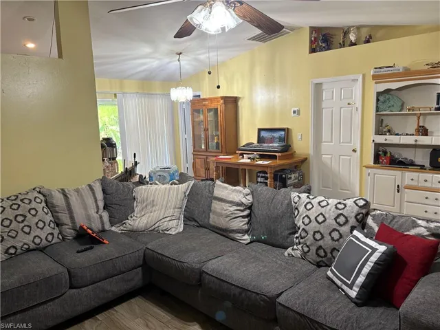 Living area featuring vaulted ceiling, ceiling fan, a chandelier, and wood finished floors