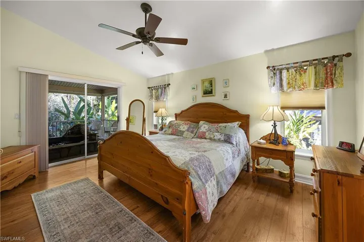Bedroom with access to exterior, vaulted ceiling, hardwood / wood-style floors, and a ceiling fan