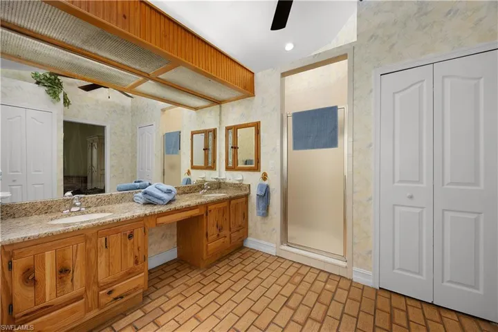 Bathroom with wallpapered walls, a closet, a ceiling fan, brick floors, and double vanity