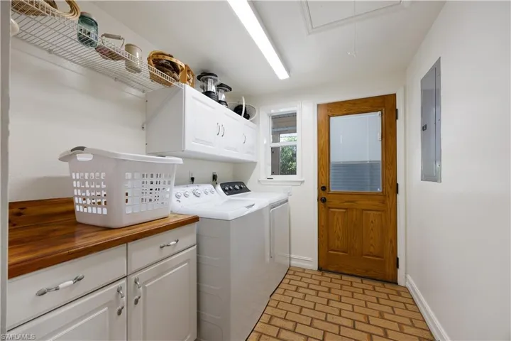 Laundry room with brick flooring, cabinet space, washer and dryer, and electric panel