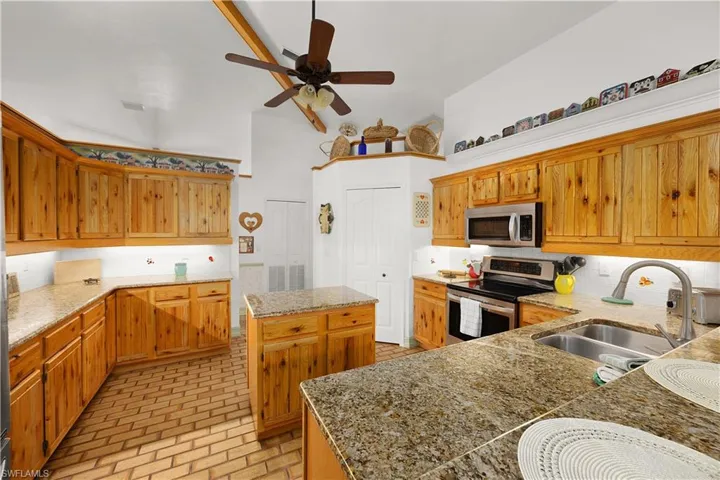 Kitchen with stainless steel appliances, a center island, dark stone countertops, brick patterned floors, and ceiling fan