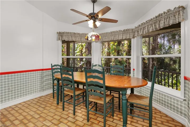 Dining space featuring wallpapered walls, a ceiling fan, brick flooring, and wainscoting