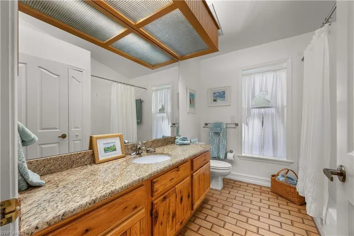 Full bath featuring vanity, vaulted ceiling, brick flooring, and curtained shower