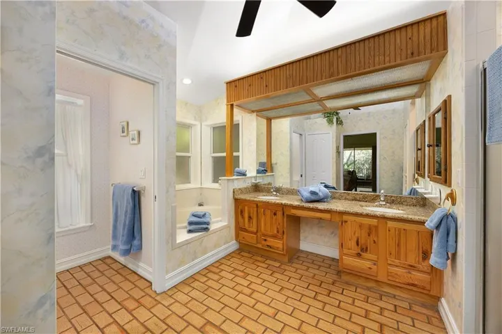 Bathroom featuring wallpapered walls, brick flooring, double vanity, ceiling fan, and a garden tub
