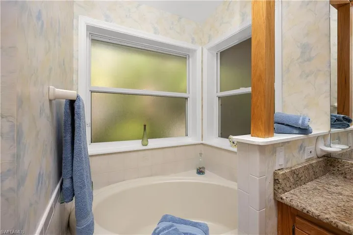Bathroom featuring a bath, wallpapered walls, and vanity