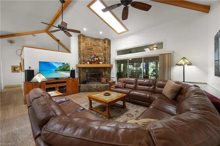Living room featuring ceiling fan, lofted ceiling, a stone fireplace, and wood finished floors